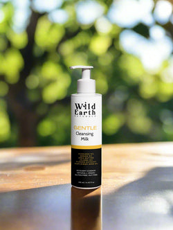 Wild Earth Gentle Cleansing Milk bottle on a wooden surface with a blurred green background